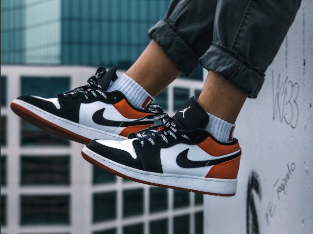 Paire de baskets Air Jordan 1 Low noir, blanc et orange, portée sur un rebord en béton.